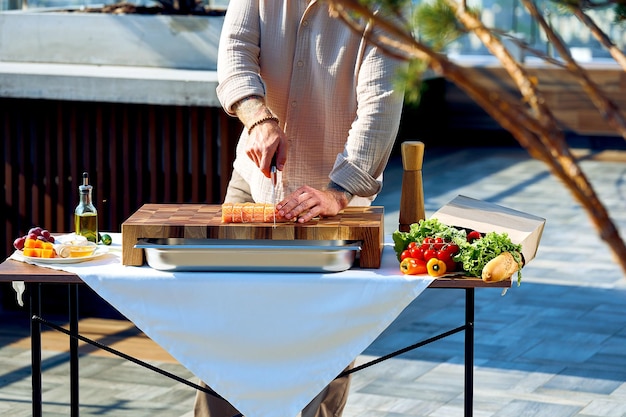 Le chef prépare des steaks de saumon sur une planche de bois dans une terrasse d'été. Préparation pour le dîner