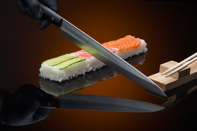 Le chef prépare des sushis, des coupes avec un couteau. sushi sur fond rouge avec reflet