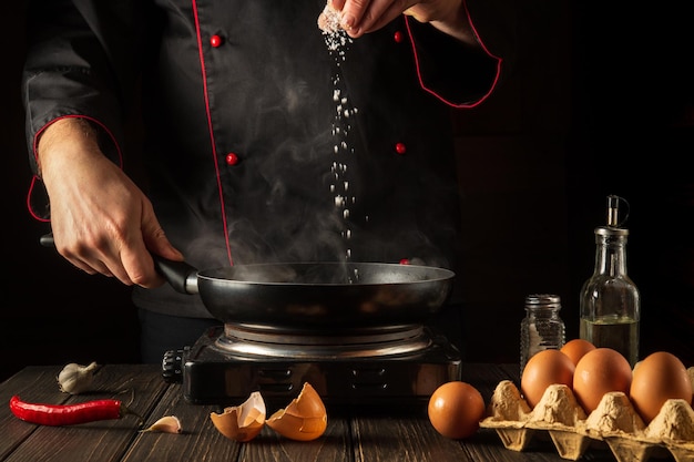 Le chef professionnel ajoute du sel pendant la cuisson des œufs dans la poêle