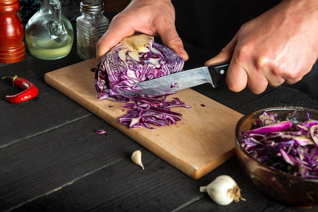 Chef professionnel coupant le chou rouge avec un couteau Cuisson de la salade de légumes dans la cuisine