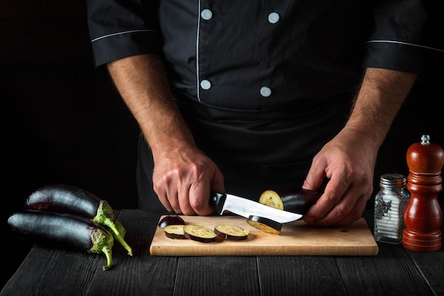 Le chef professionnel coupe une aubergine dans la cuisine Gros plan des mains du cuisinier pendant le travail