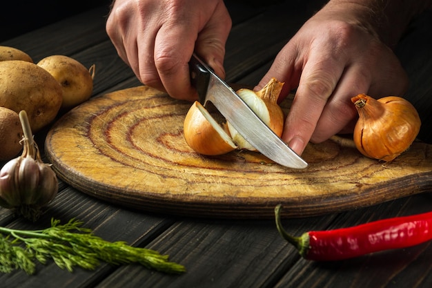 Le chef professionnel coupe l'oignon avec un couteau sur une planche à découper pour faire de la soupe pour le déjeuner