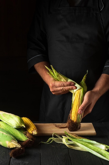 Le chef professionnel épluche le maïs mûr de la coquille avant la cuisson