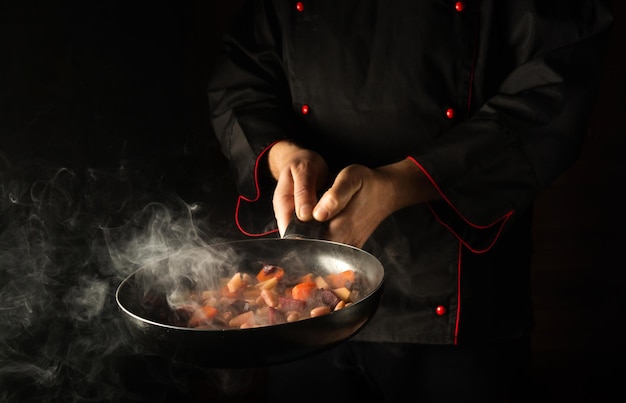 Le chef professionnel prépare la nourriture dans une poêle à frire avec de la vapeur sur un fond noir