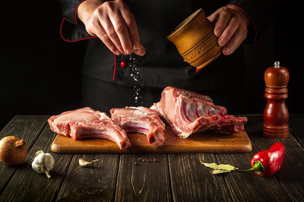 Un chef professionnel saupoudre de sel des côtes crues Le concept de cuisiner de délicieux plats pour l'hôtel