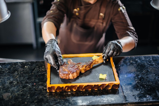 Un chef professionnel sert magnifiquement un steak grillé juteux avec du beurre et des assaisonnements. Viande grillée dans un restaurant.
