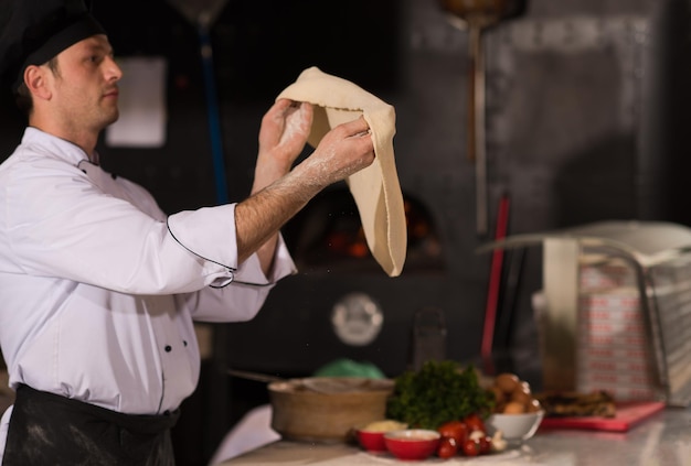 Chef qualifié préparant la pâte pour la pizza roulant avec les mains et vomissant