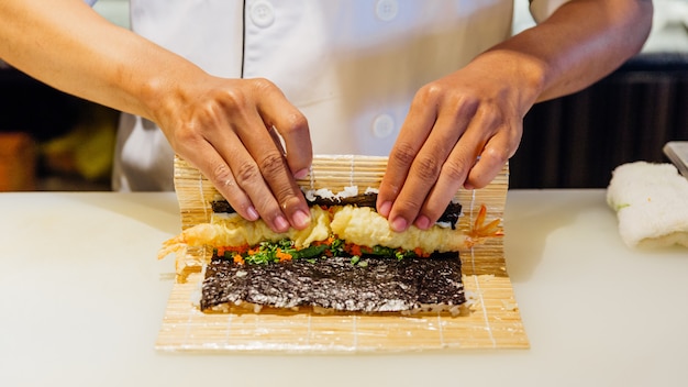 Chef roulant maki sushi avec riz, tempura de crevettes, avocat et fromage à l'intérieur de la farine croustillante recouverte de croustillant.