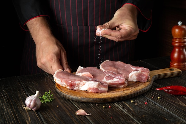 Le chef sale des steaks de viande tranchés crus sur la planche à découper de la cuisine du restaurant avant de préparer le dîner Délicieuse idée de grillades