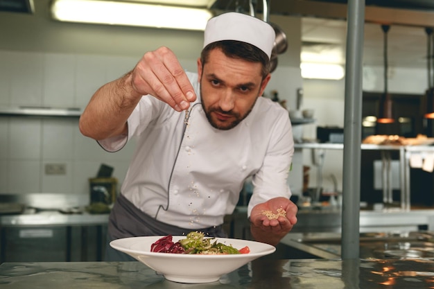 Photo le chef saupoudre de sel une salade de légumes frais dans la cuisine du restaurant nourriture savoureuse et saine