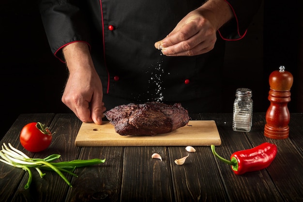 Le chef saupoudre la viande de boeuf cuite au four avec du sel Environnement de travail sur la table de la cuisine Cuisine asiatique