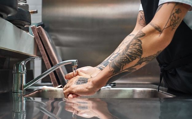 le chef se lave soigneusement les mains avec différents tatouages dans une cuisine de restaurant