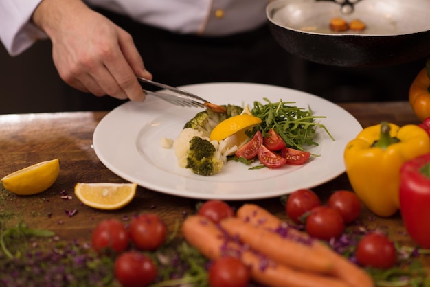 Photo chef servant une salade de légumes sur une assiette dans la cuisine du restaurant