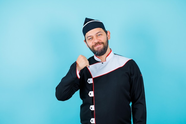 Le chef souriant regarde la caméra en levant le poing sur fond bleu