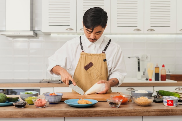 Chef de sushi faisant des rouleaux sur une planche à découper dans la cuisine divers ingrédients autour