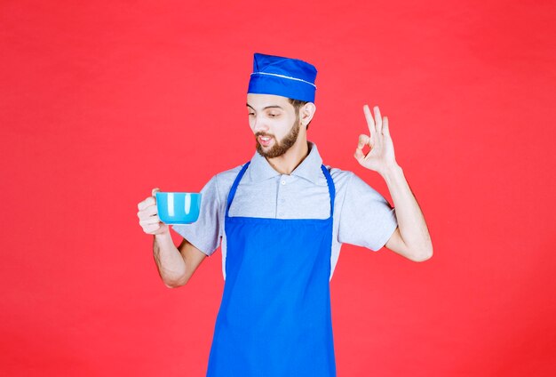 Photo chef en tablier bleu tenant une tasse en céramique bleue et appréciant le goût du produit.