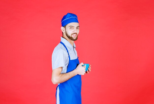 Chef en tablier bleu tenant une tasse en céramique bleue.