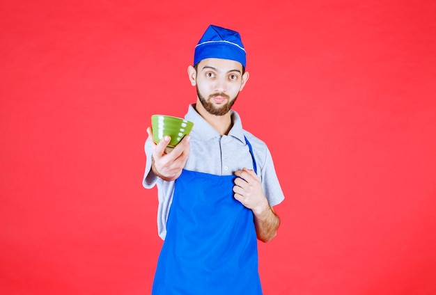 Chef en tablier bleu tenant une tasse en céramique verte.