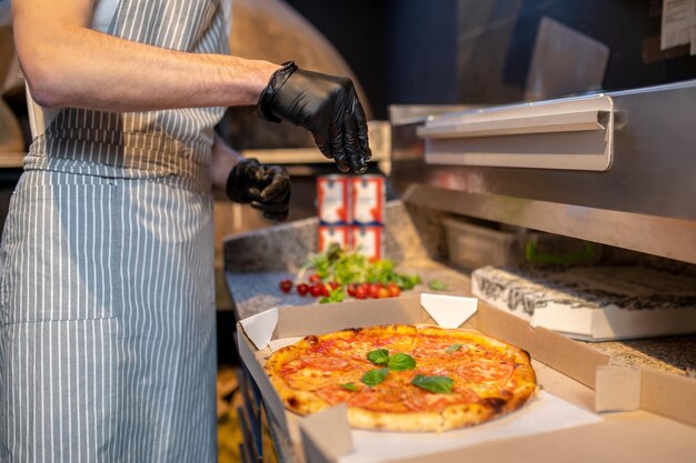 Un chef en tablier et bonnet de cheveux préparant une pizza