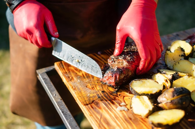 Chef tatoué avec des gants en caoutchouc hachant un steak grillé à l'extérieur