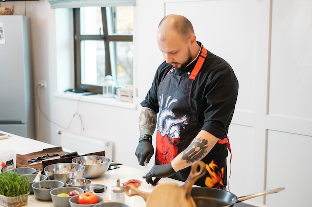 Photo un chef tatoué en gants noirs sculpte la viande couper la viande hachée avec un couteau dans une cuisine moderne