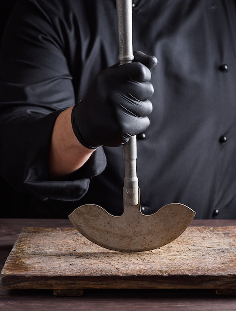 Chef en tenue noire tient à la main un vieux couteau en métal