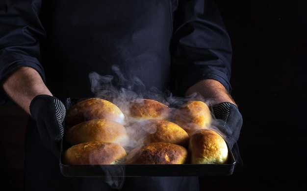 Le chef tient une plaque à pâtisserie avec des petits pains ou des tartes fraîchement cuits Espace noir pour le menu ou la recette