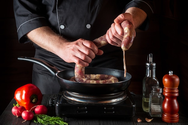 le chef tient la saucisse de viande crue avant de cuisiner l'environnement de travail dans une cuisine de restaurant