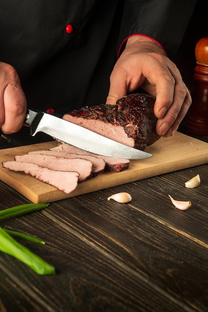 Le chef tranche le steak de boeuf avec un couteau sur une planche à découper en bois Vue de dessus