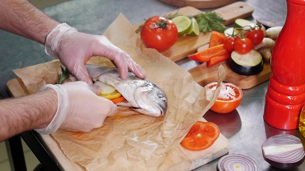 Un chef travaillant dans la cuisine remplissant le poisson de légumes et graissant le poisson avec une huile