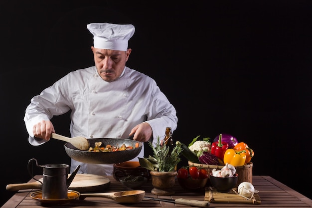 Chef en uniforme blanc et chapeau avec louche mélange les ingrédients sur la plaque de cuisson