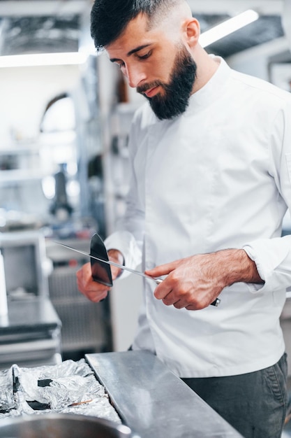 Chef en uniforme blanc debout à la cuisine tenant des couteaux dans les mains