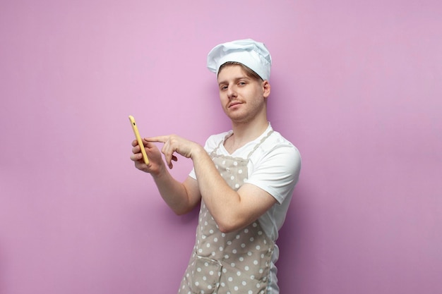 Chef en uniforme et chapeau utilise un smartphone et touche l'écran avec le doigt sur fond rose