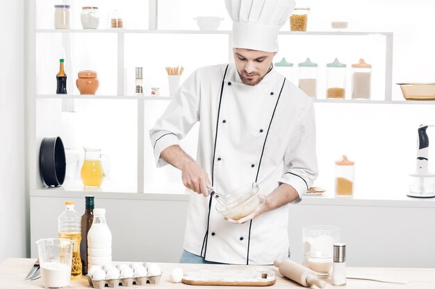 Le chef en uniforme fait de la pâte dans la cuisine