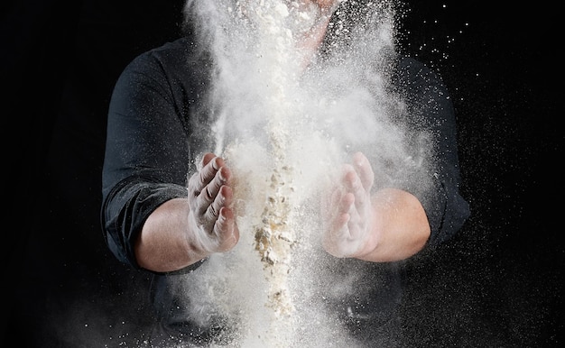 Photo le chef en uniforme noir répand de la farine de blé blanc dans différentes directions.