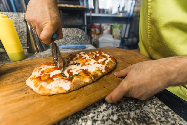 Chef en uniforme vert salade tranchant de la pizza à la boulangerie