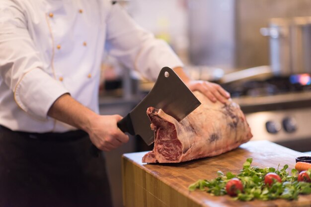 chef utilisant une hache tout en coupant un gros morceau de bœuf sur une planche de bois dans la cuisine du restaurant