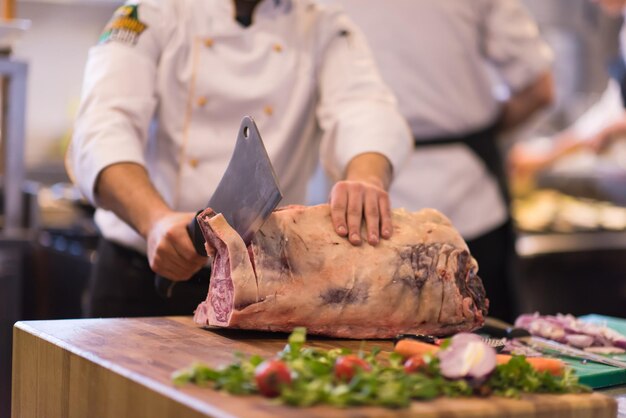 chef utilisant une hache tout en coupant un gros morceau de bœuf sur une planche de bois dans la cuisine du restaurant