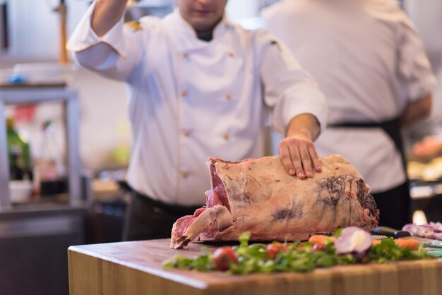 chef utilisant une hache tout en coupant un gros morceau de bœuf sur une planche de bois dans la cuisine du restaurant