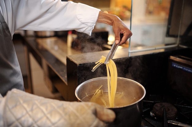 Chef utilisant des pincettes de cuisine pour vérifier si les pâtes sont cuites