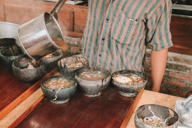 Chef utilisant l'uniforme Lurik versant une soupe dans le soto bathok à Yogyakarta