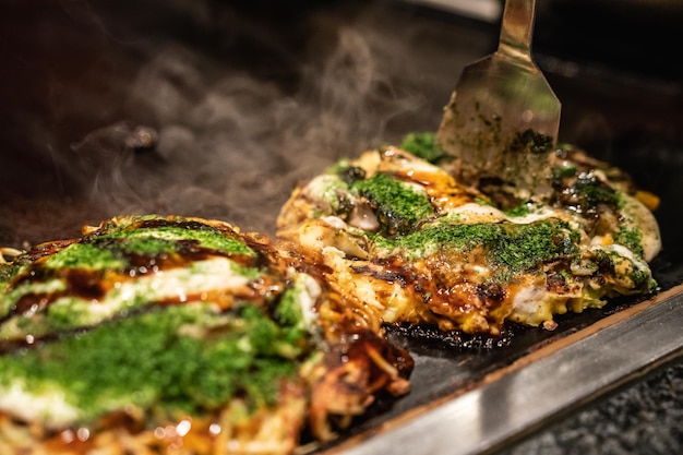 le chef utilise une spatule pour couper l'okonomiyaki fait en deux sur la plaque de fer, et prêt à donner la délicieuse cuisine traditionnelle japonaise aux clients