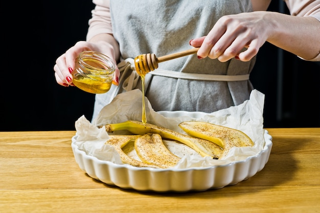 Le chef verse des tranches de banane au miel dans un plat allant au four. Cuisson des bananes frites.