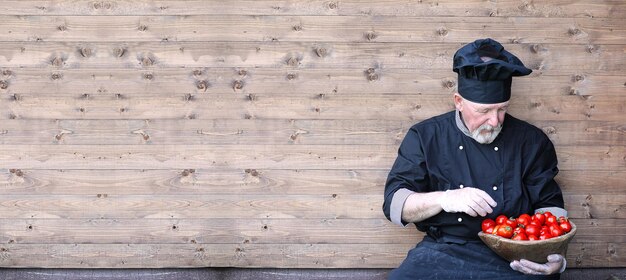 Chef vieux en uniforme avec des légumes frais sur un fond en bois