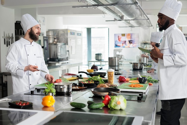 Les chefs discutent du repas à préparer pour le service du dîner au restaurant gastronomique. Divers travailleurs de l'industrie alimentaire discutent de la recette de plats gastronomiques tout en cuisinant dans une cuisine professionnelle.