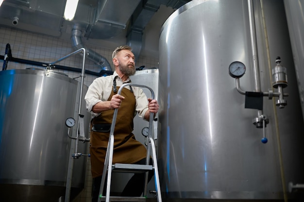 Échelle ascendante de brasseur d'homme contre le navire en métal dans l'usine de bière