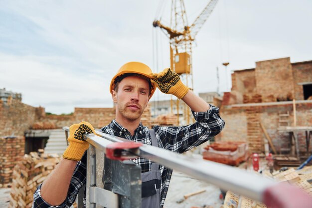 Échelle dans les mains Ouvrier du bâtiment en uniforme et équipement de sécurité a un travail sur la construction