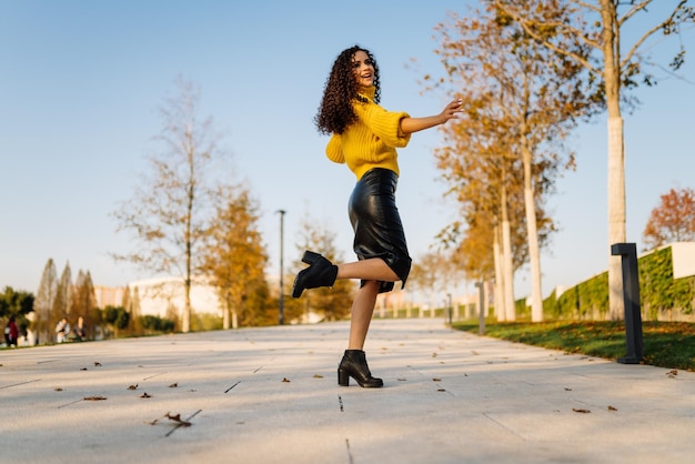 Sur le chemin du parc à l39automne se dresse levant une jambe pliée au genou se tient une fille posant dans une jupe en cuir et un pull brillant