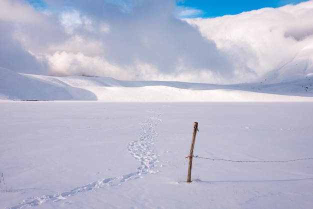 Chemin d'empreintes de paysage d'hiver et clôture sur la vallée de neige en journée ensoleillée