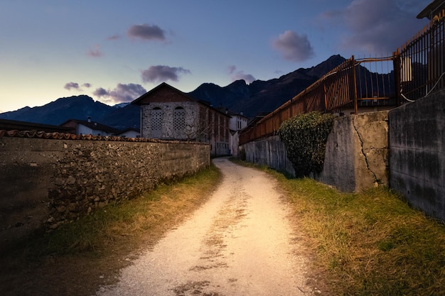 Chemin de terre entre les vieilles maisons au coucher du soleil, montagnes en arrière-plan, Santa Giustina, Belluno